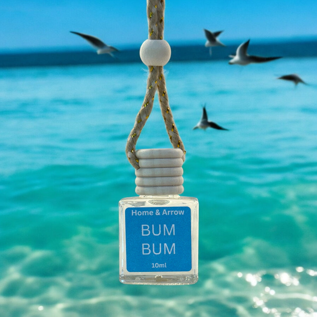Small bottle labeled 'BUM BUM' by Home & Arrow hanging in clear blue water with seagulls in the background.