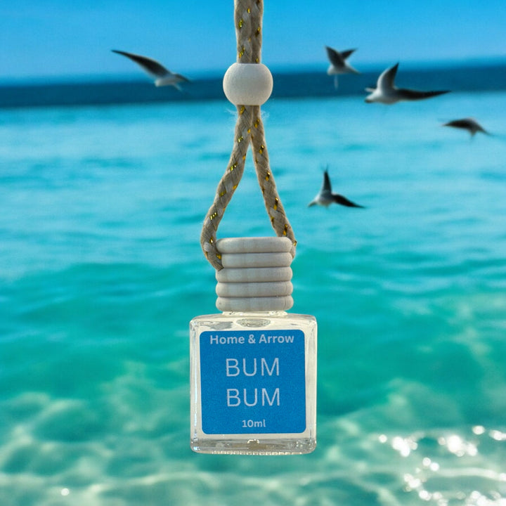 Small bottle labeled 'BUM BUM' by Home & Arrow hanging in clear blue water with seagulls in the background.