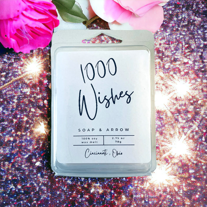 Pink flowers and glitter background featuring a '1000 Wishes' wax melt in clamshell packaging, labeled 100% soy wax melt from Home & Arrow in Cincinnati, Ohio