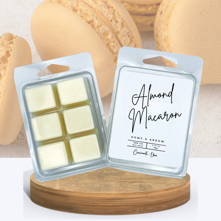 Almond Macaron wax melts in clamshell packaging, displayed on a wooden stand with several almond colored macaron cookies in the background.