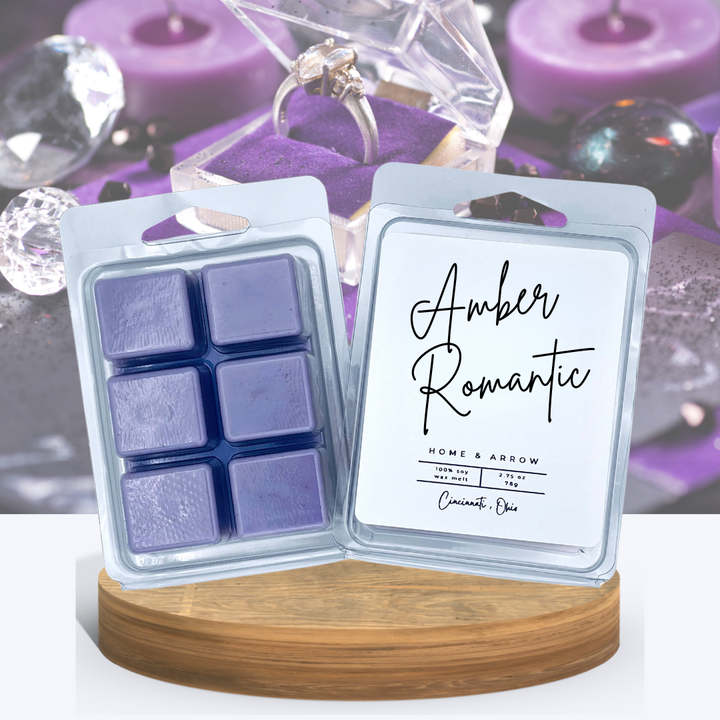 Purple 'Amber Romantic' soy wax melt clamshells displayed on a wooden stand with jewelry and candles in the background.