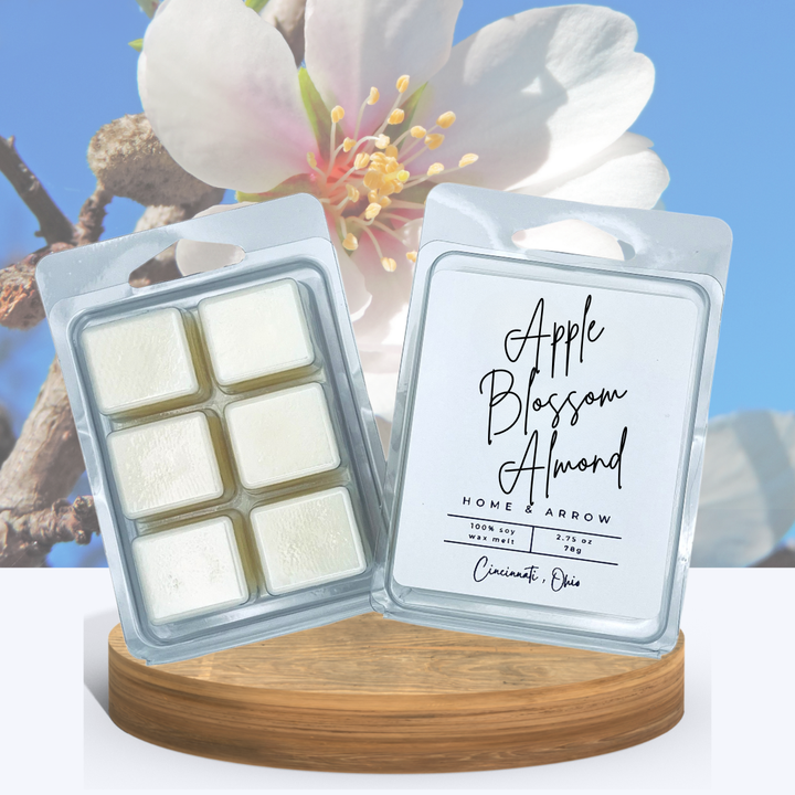 Apple Blossom Almond soy wax melts in clamshell packaging, displayed on a wooden stand with a blooming flower background.