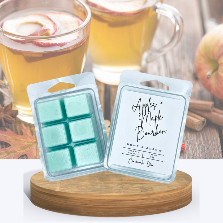 Apples + Maple Bourbon soy wax melts in clamshell packaging, displayed on a wooden stand with apple cider and autumn-themed background.