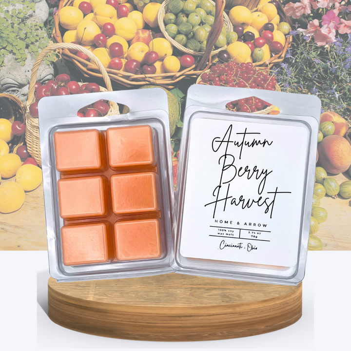 Autumn Berry Harvest soy wax melts in clamshell packaging, displayed on a wooden stand with a background of baskets filled with fresh berries and fruits.