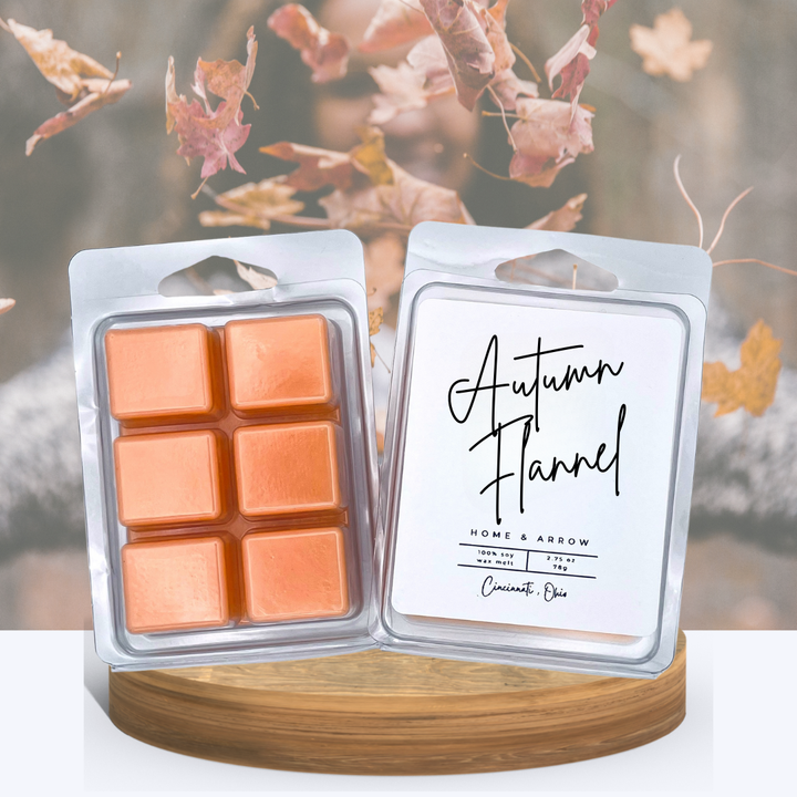 Autumn Flannel soy wax melts in clamshell packaging, displayed on a woode stan with a girl in a flannel sweater and leaves falling in the background. 