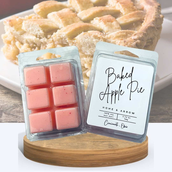 Baked Apple Pie soy wax melts in clamshell packaging, displayed on a wooden stand with a slice of apple pie in the background.