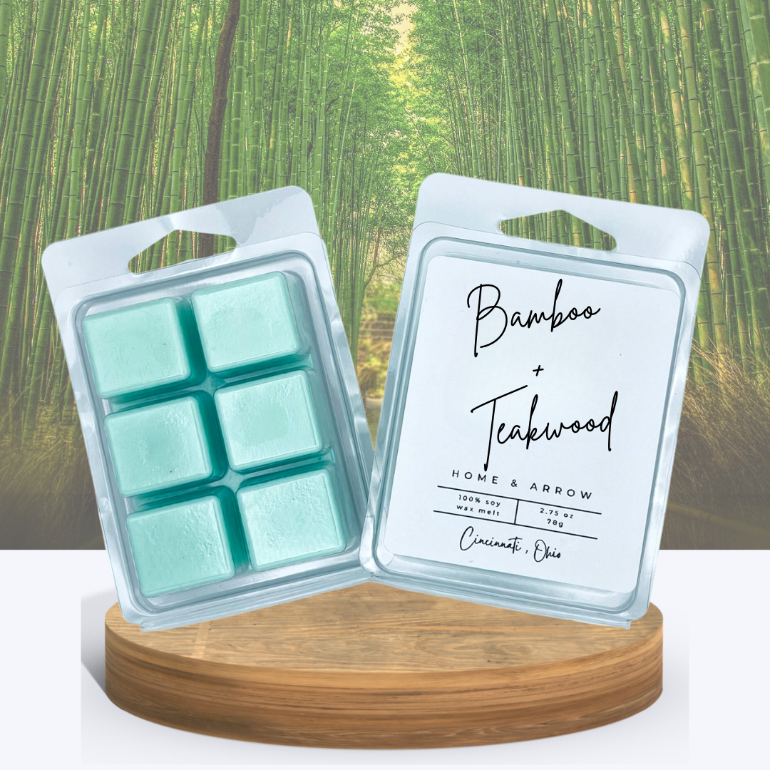 Bamboo + Teakwood soy wax melts in clamshell packaging, displayed on a wooden stand with a bamboo forest background.