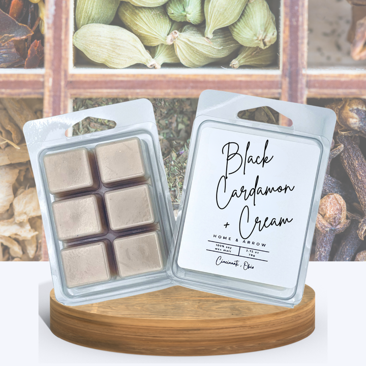 Black Cardamon + Cream soy wax melts in a clamshell package, displayed on a wooden stand with a wooded box of spices in the background.