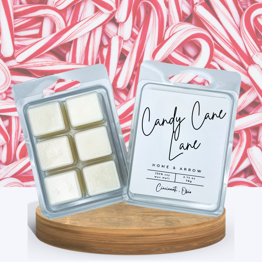 Candy Cane Lane soy wax melts in a clamshell package dispayed on a wooden stand with a pile of candy canes in the background. 