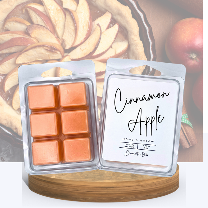 Cinnamon Apple orange wax melts in clamshell packaging, displayed on a wooden stand with several almond colored macaron cookies in the background.