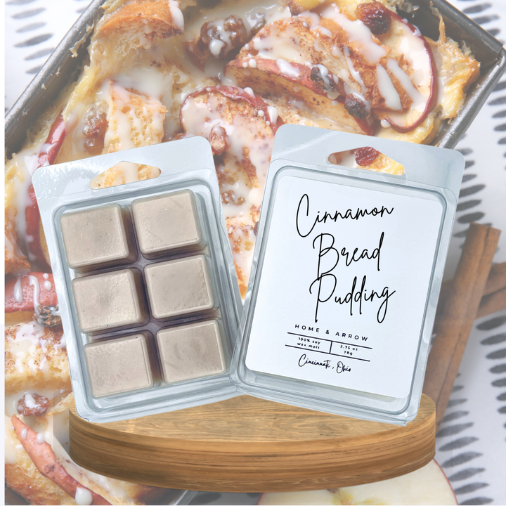 Two wax melts in clear clamshell packaging are shown in front of a cinnamon bread pudding dish. The left package contains six beige wax melts, and the right package is labeled 'Cinnamon Bread Pudding' by Home & Arrow.