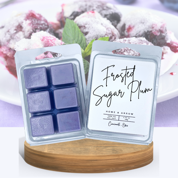 Frosted Sugar Plum purple wax melts in clamshell packaging, displayed on a wooden stand with several almond colored macaron cookies in the background.