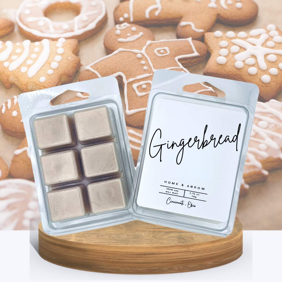  Gingerbread wax melts in clamshell packaging displayed on a wooden stand with decoraged gingerbread cookies in the background.