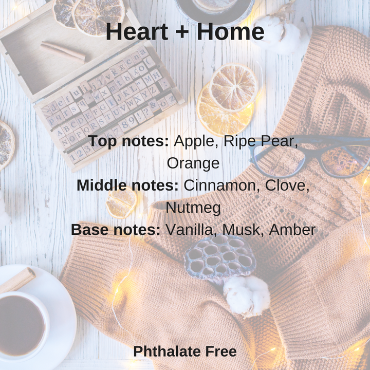 A wax melt cube from Heart + Home brand placed on a wooden surface with a knitted texture, surrounded by items suggesting a cozy home atmosphere, such as a cup of tea, lemon slices, and a book.