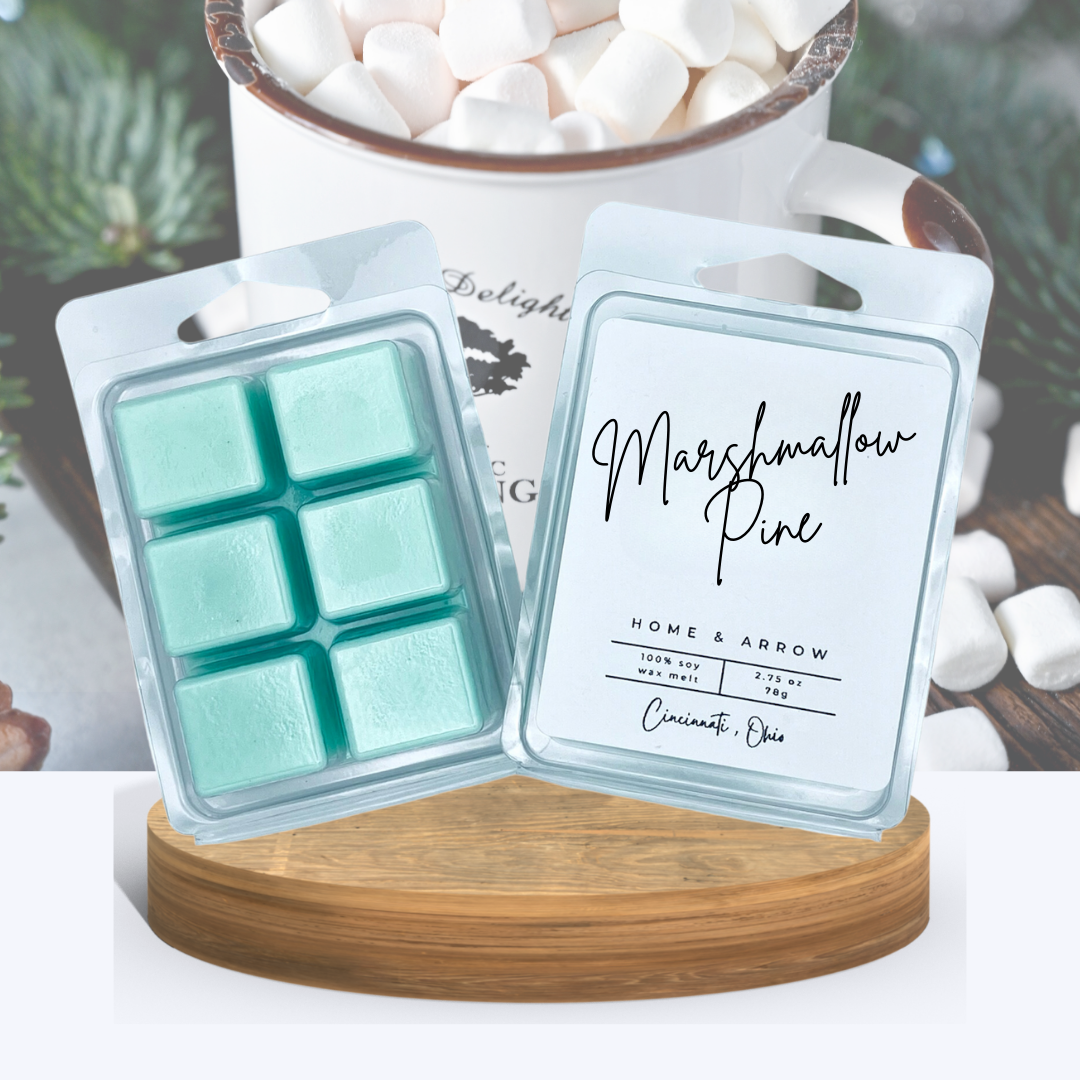 Marshmallow Pine wax melts in clamshell packaging, displayed on a wooden stand with a cup of marshmallows in a tin cup in front of pine leaves.