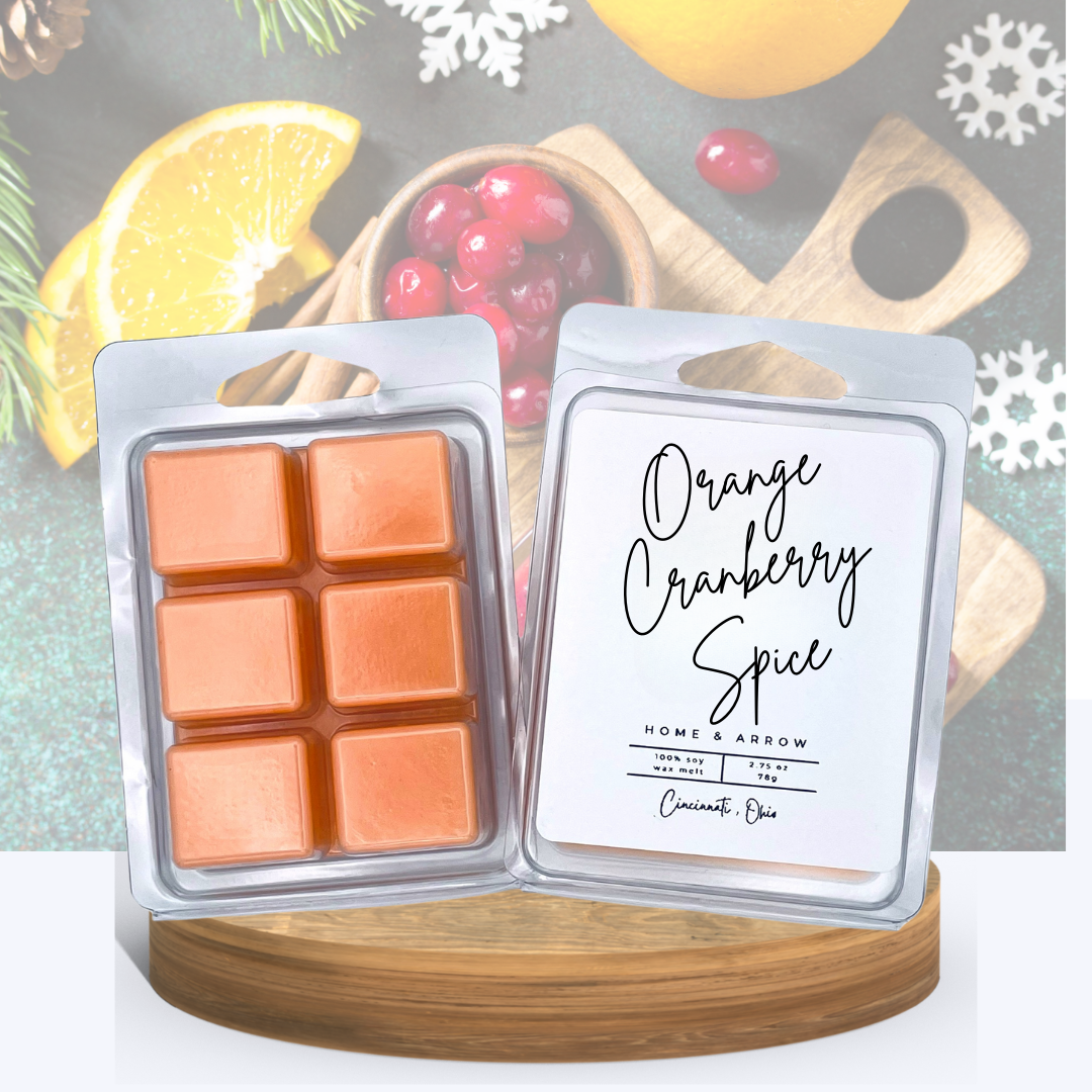 Orange Cranberyy Spice soy wax melt in a clamshell package, displayed on a wooden stand with festive holiday serving board in the background.