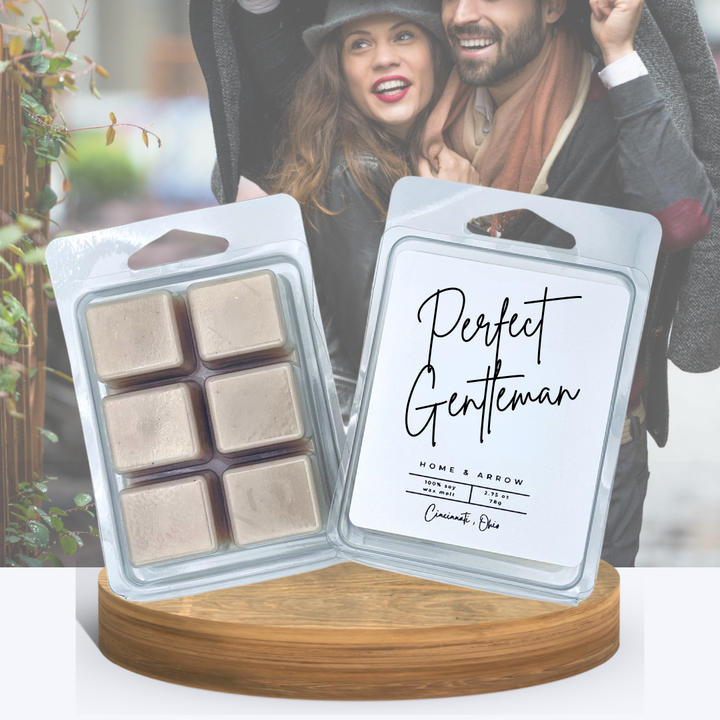 Perfect Gentleman wax melts in clamshell packaging displayed on a wooden stand with a couple in the rain and the man is holding a jacket over them both. 