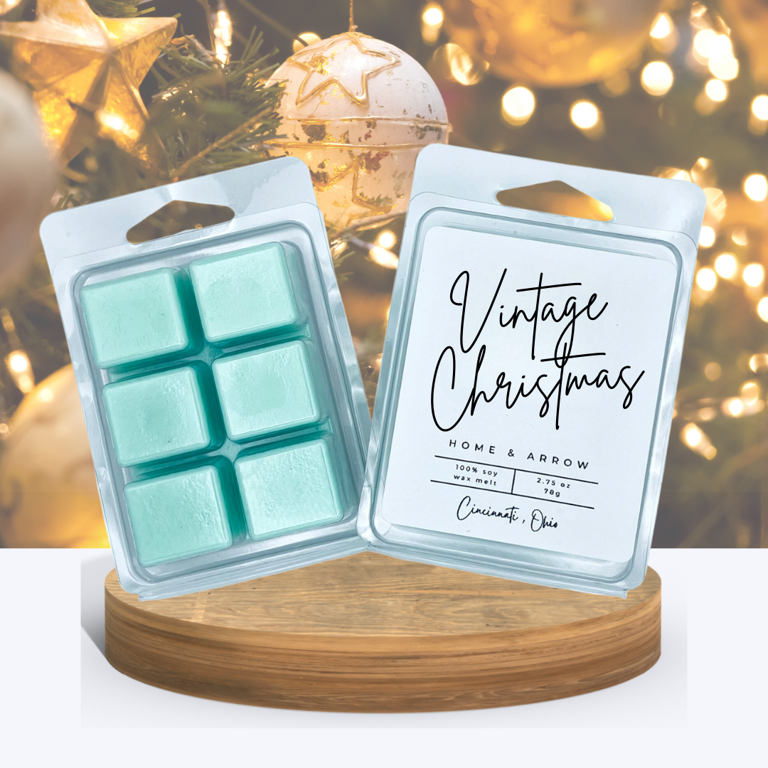 Vintage Christmas wax melts in clamshell packaging displayed on a wooden stand with a golden lit christmas tree in the background.